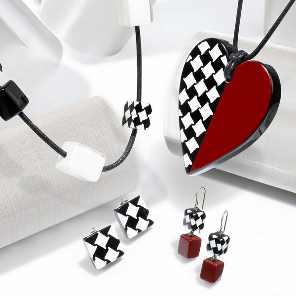 November collection — Black-and-white houndstooth meeting a single solid half in navy, deep red or ivory, across hearts, cubes and neat studs.
